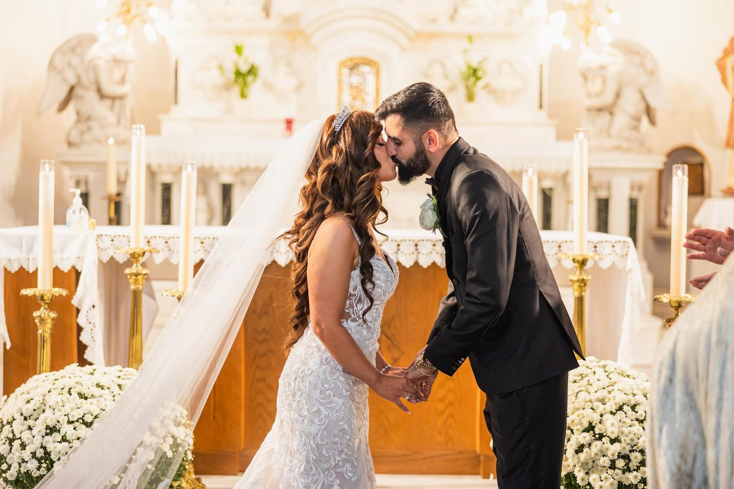 Intimate wedding ceremony moment at decorated church altar with white flowers.