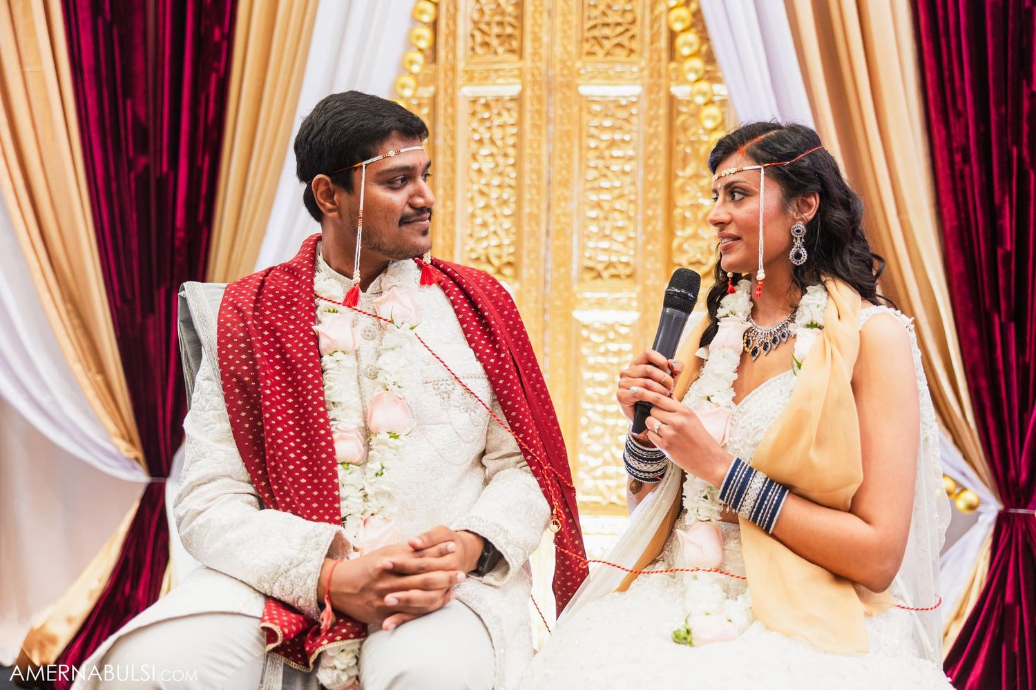A couple shares a light moment during their Indian wedding ceremony on stage.