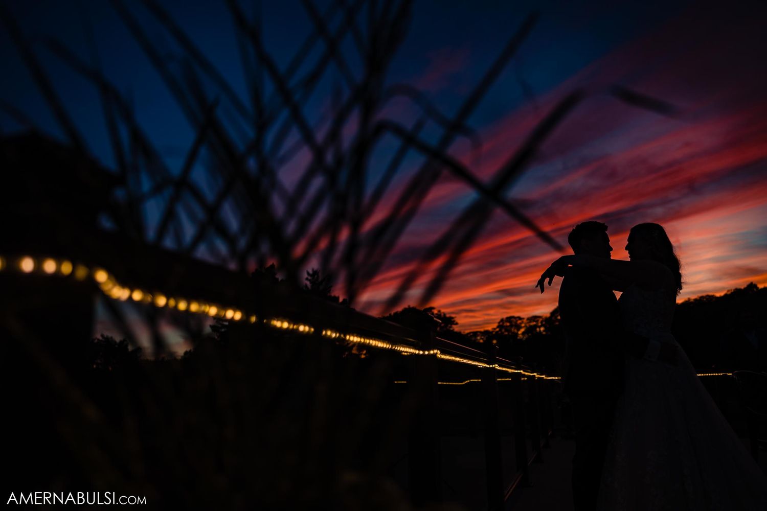 A silhouetted couple stands against a vibrant orange and purple sunset sky.
