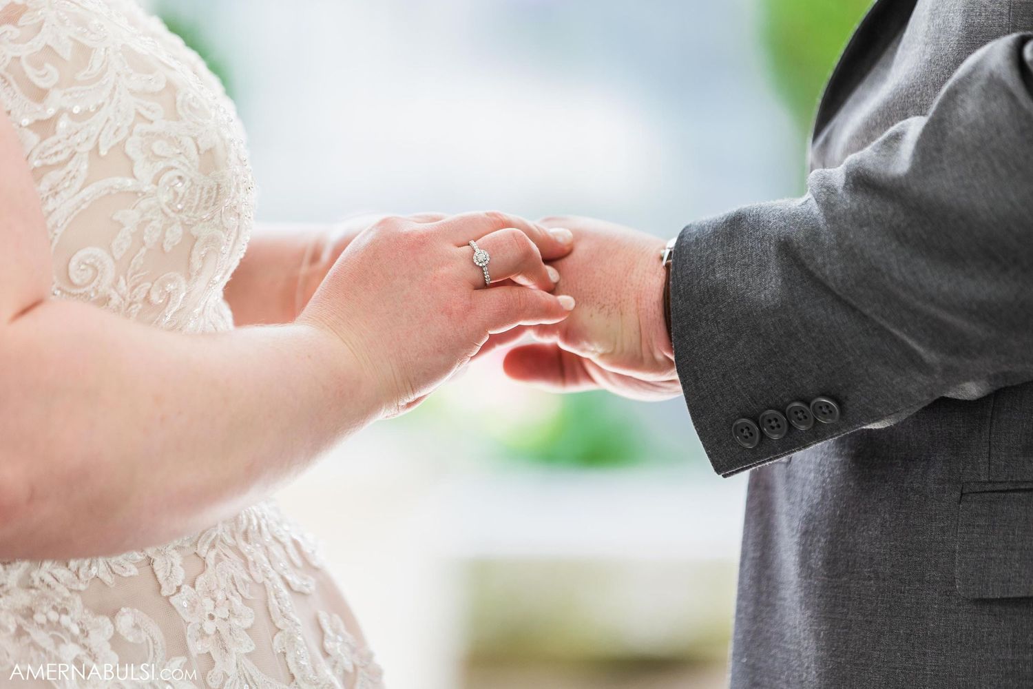 Close-up of bride and groom holding hands during outdoor wedding ceremony.
