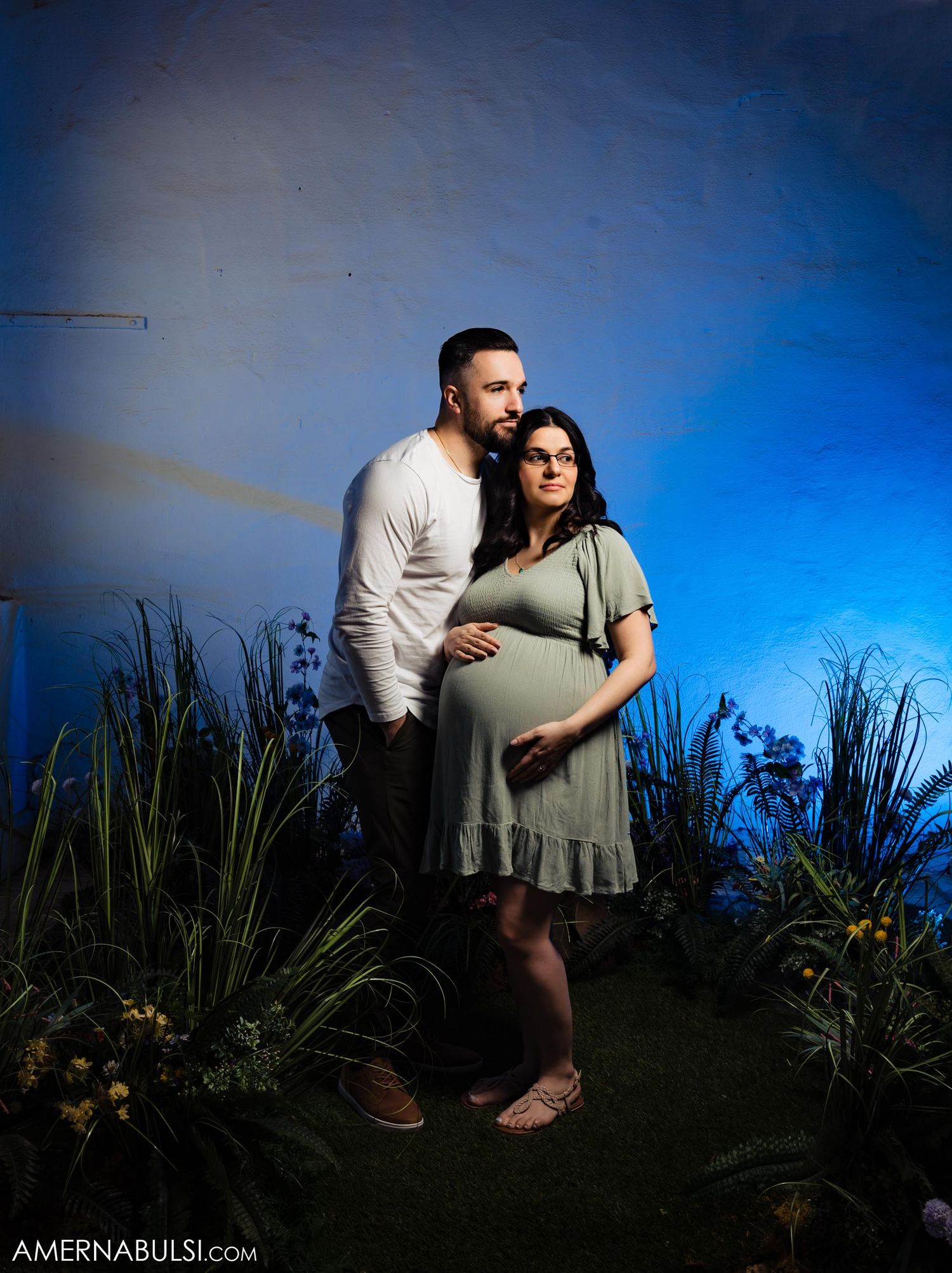 A dramatic maternity portrait with dramatic blue lighting and natural elements.