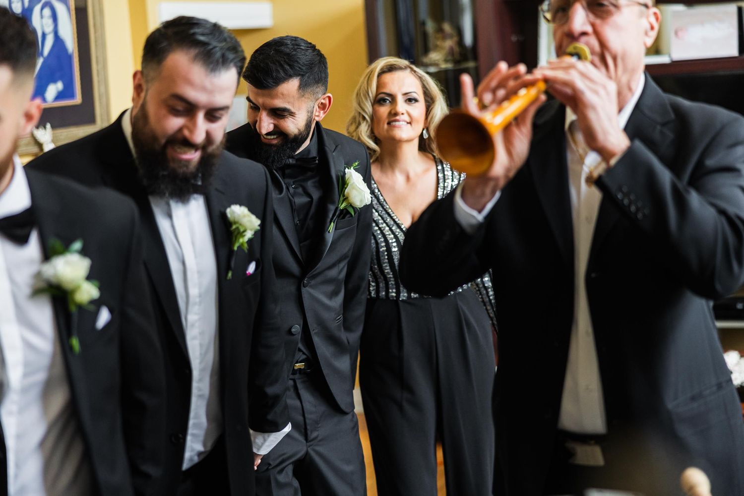 Wedding party members in black tuxedos share a candid moment during celebrations.