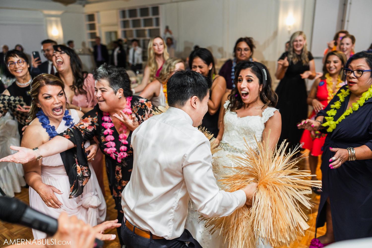 Energetic wedding celebration with guests dancing with decorative Hawaiian leis and props.