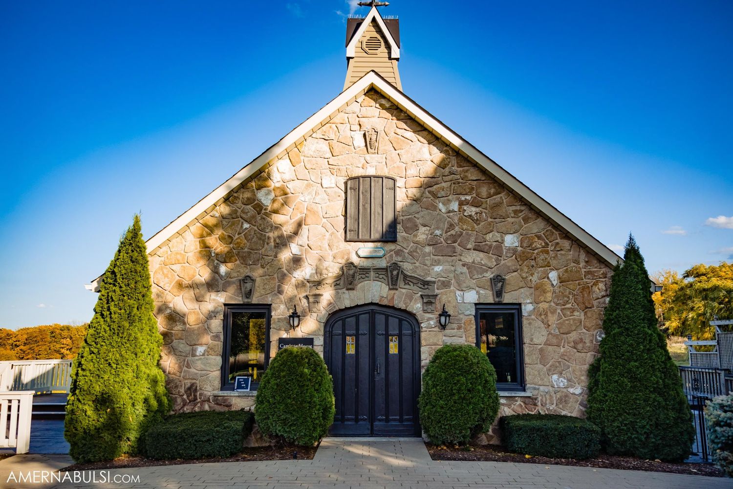 Rustic stone chapel with symmetrical topiary bushes under bright blue sky.