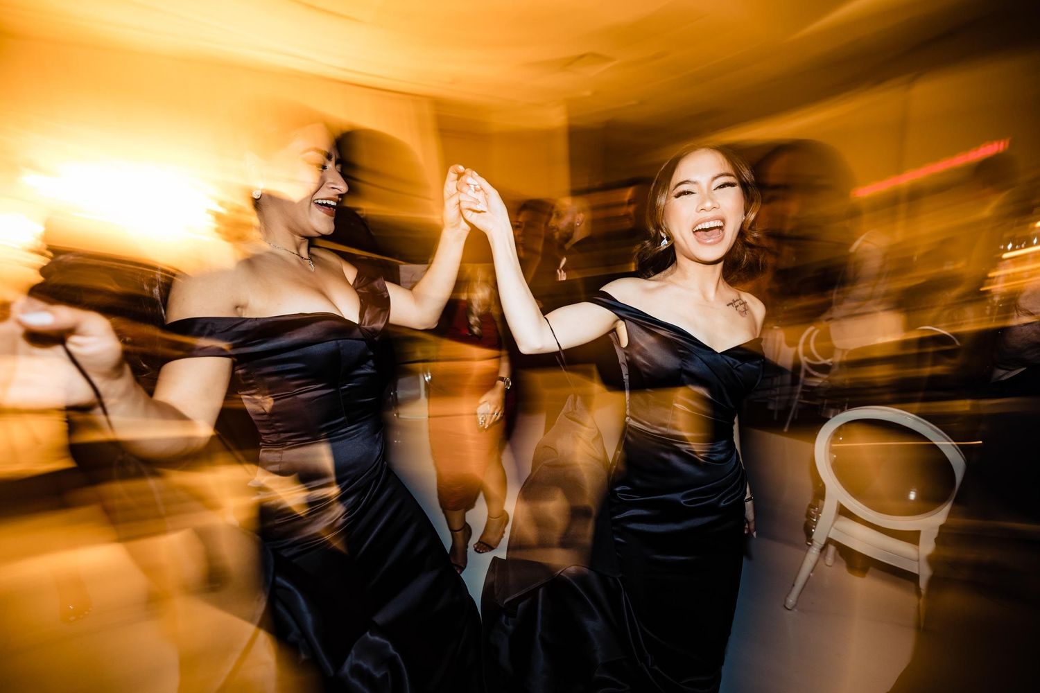 Dynamic motion blur photo of dancers in elegant black dresses at wedding reception.