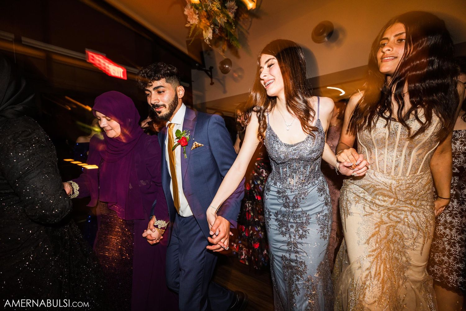 Guests in formal attire dancing in a line at an evening wedding reception.