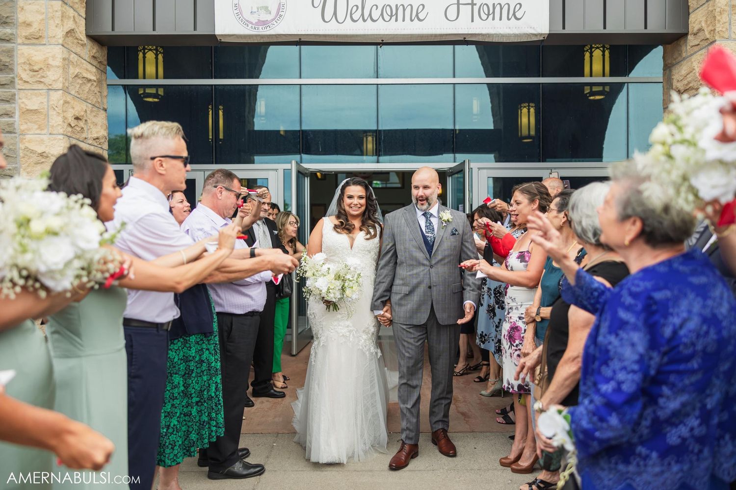Wedding ceremony exit under Welcome Home sign with celebrating guests.