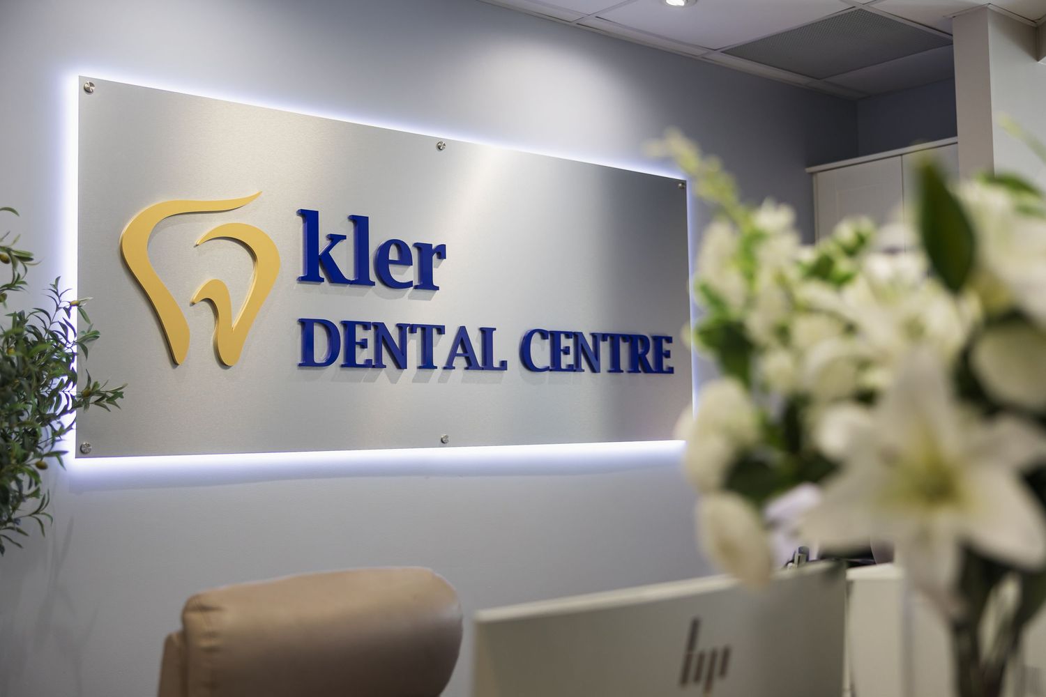 Reception desk at Kler Dental Centre with illuminated logo sign and fresh white flowers.