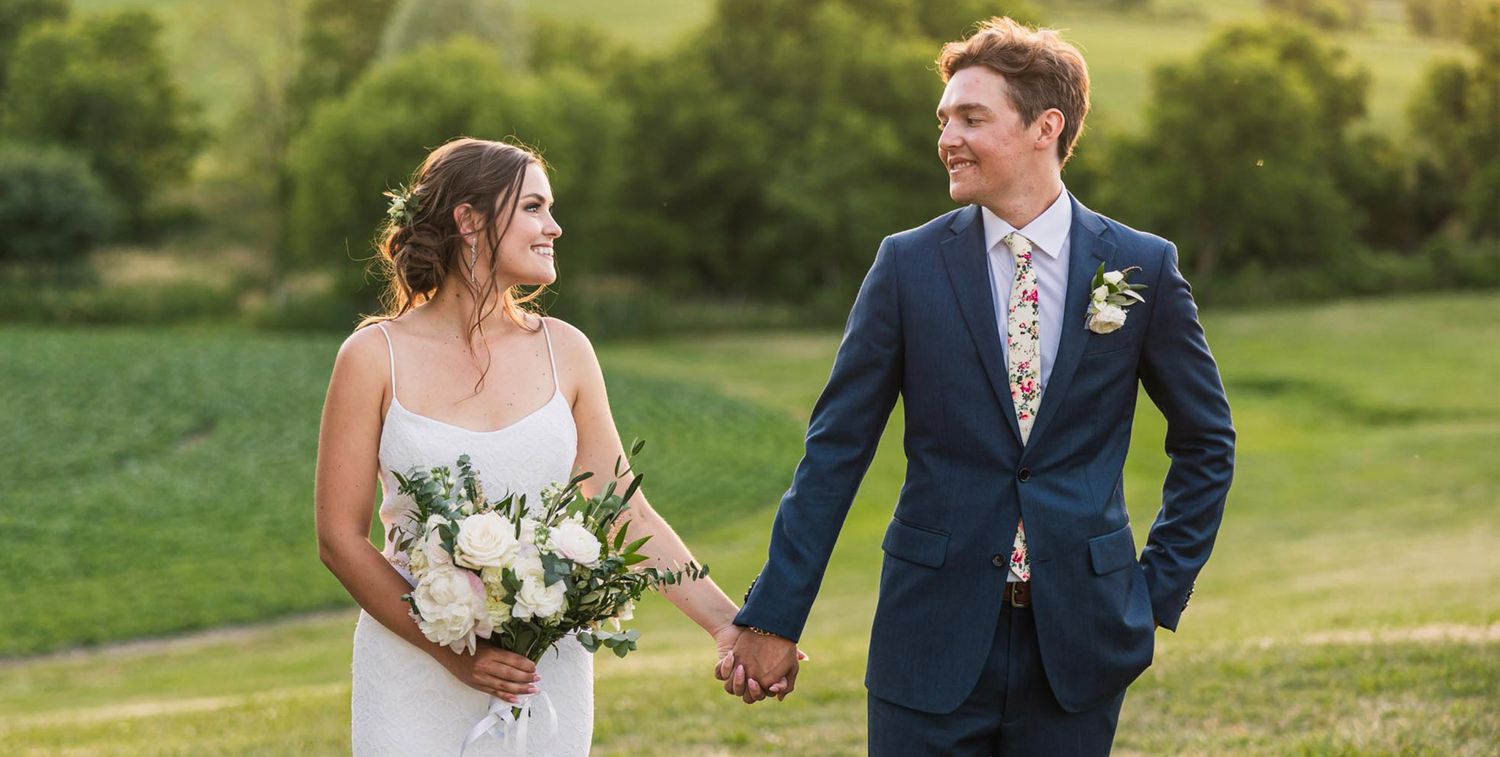 Elegant outdoor wedding photography featuring a couple walking through a lush green garden setting.