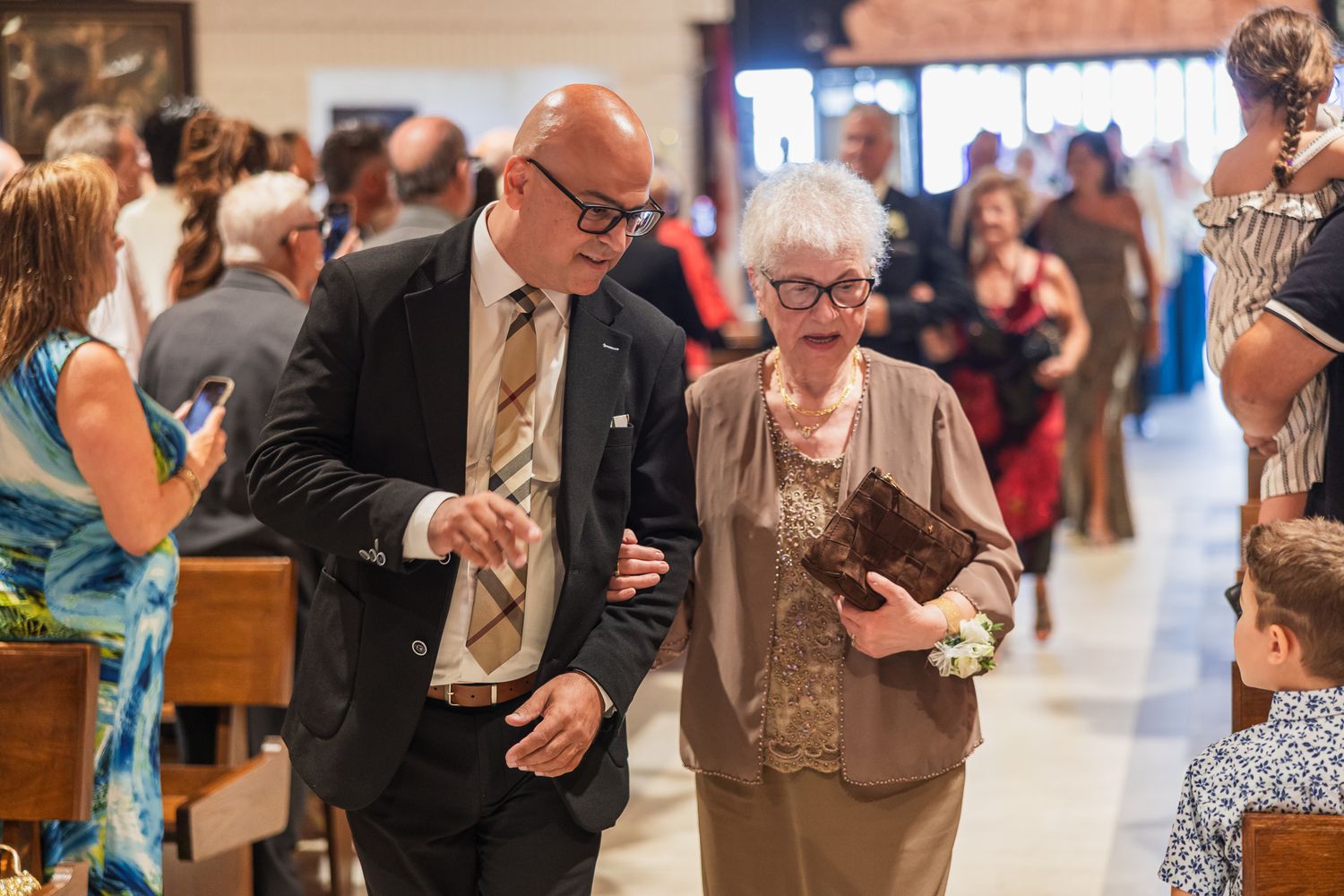 Elderly couple walks together through a crowded church foyer during a wedding reception celebration.