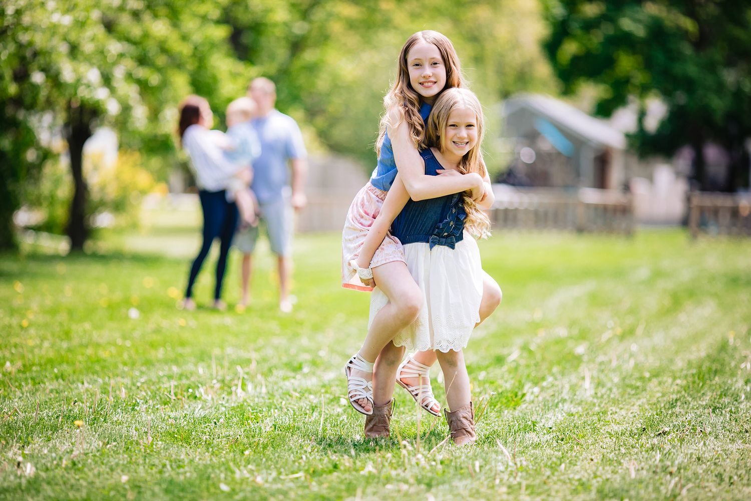 Playful piggyback ride moment in a sunny green park with others visible in background.