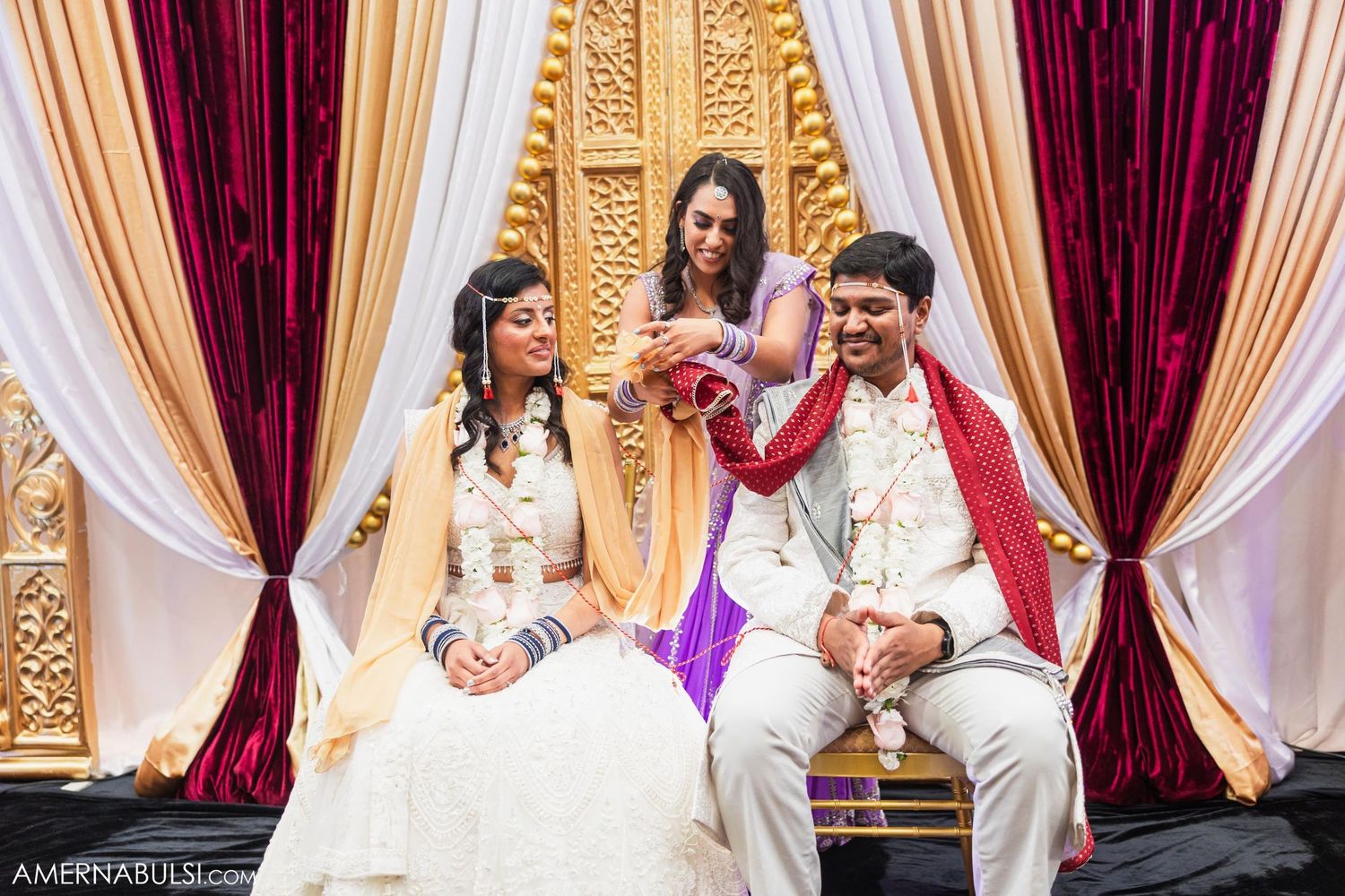 Indian wedding ceremony with bride, groom, and officiant in traditional attire on decorated golden mandap stage.