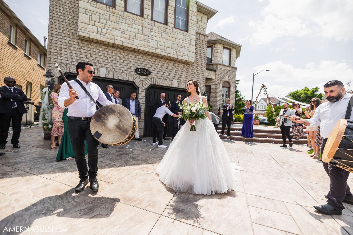 Wedding celebration outside stone building with musicians playing traditional instruments.