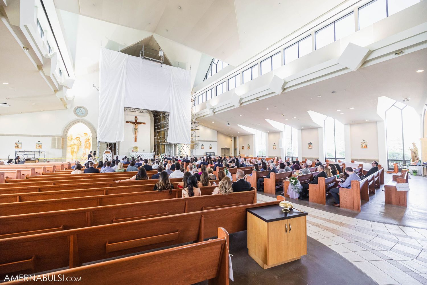 Interior view of a modern church sanctuary with wooden pews and high ceilings filled with wedding guests.