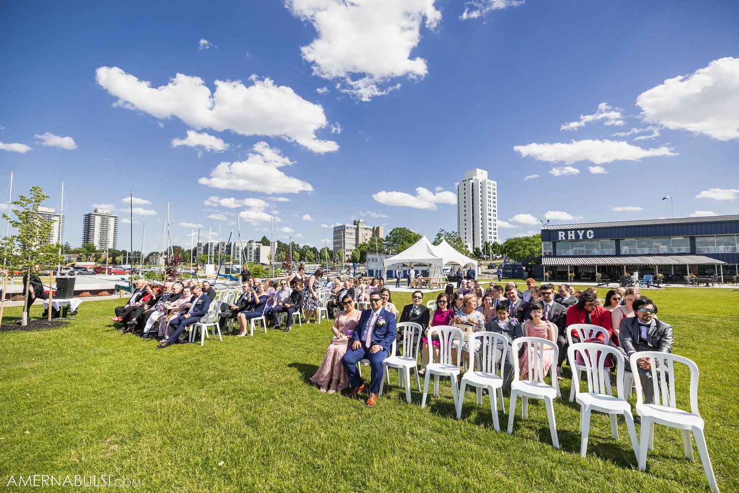 Outdoor wedding ceremony setup on green lawn with white chairs and city skyline backdrop.