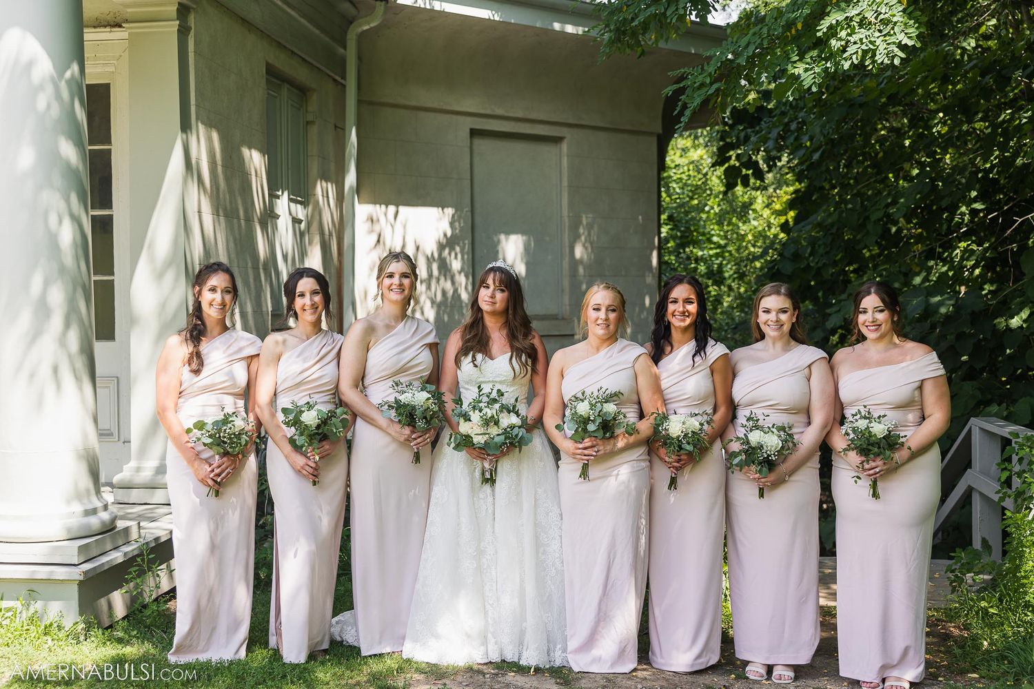 Bridesmaids in pale pink dresses standing in a row holding white floral bouquets.
