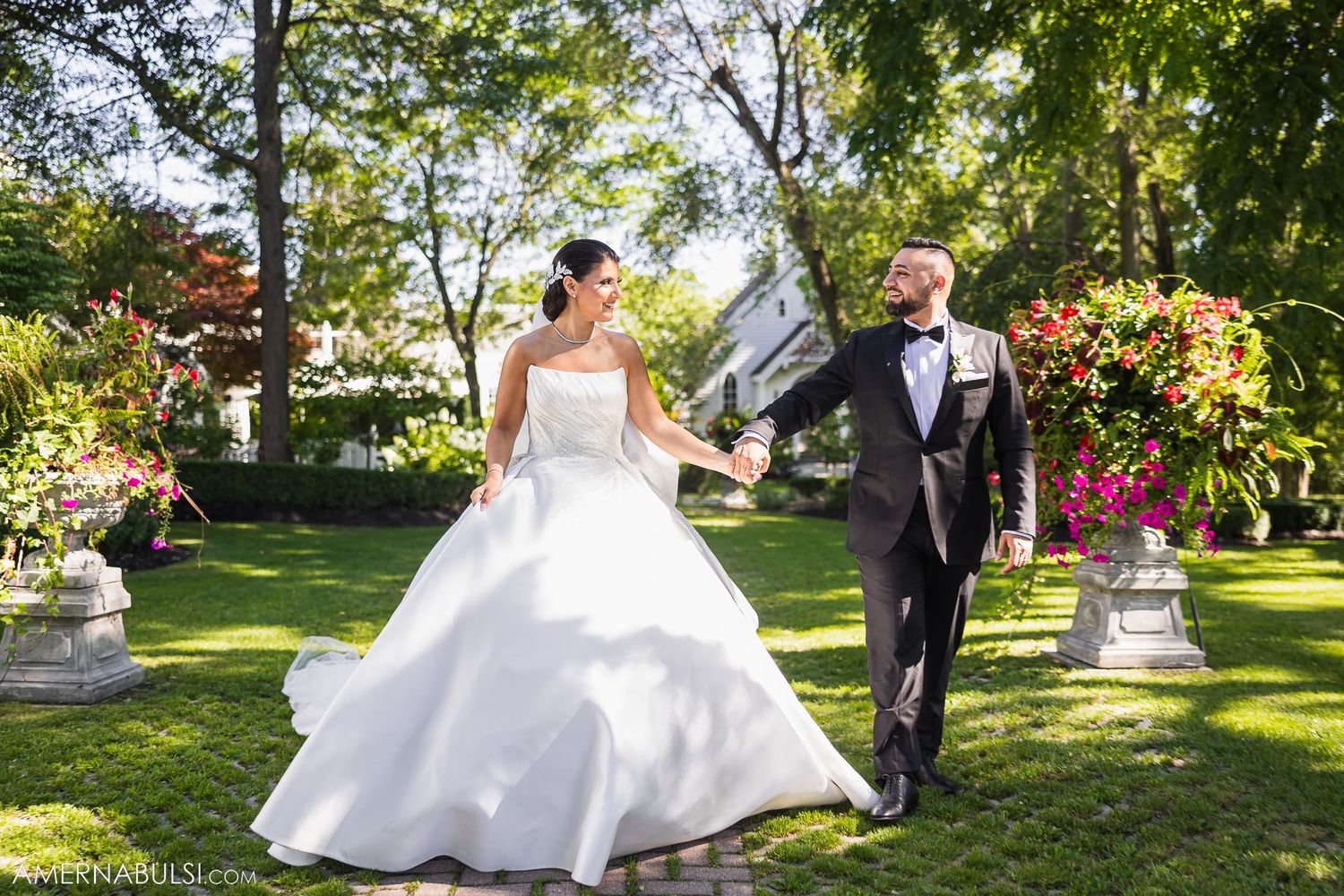 A couple walks together through a manicured garden with flowing bridal veil.