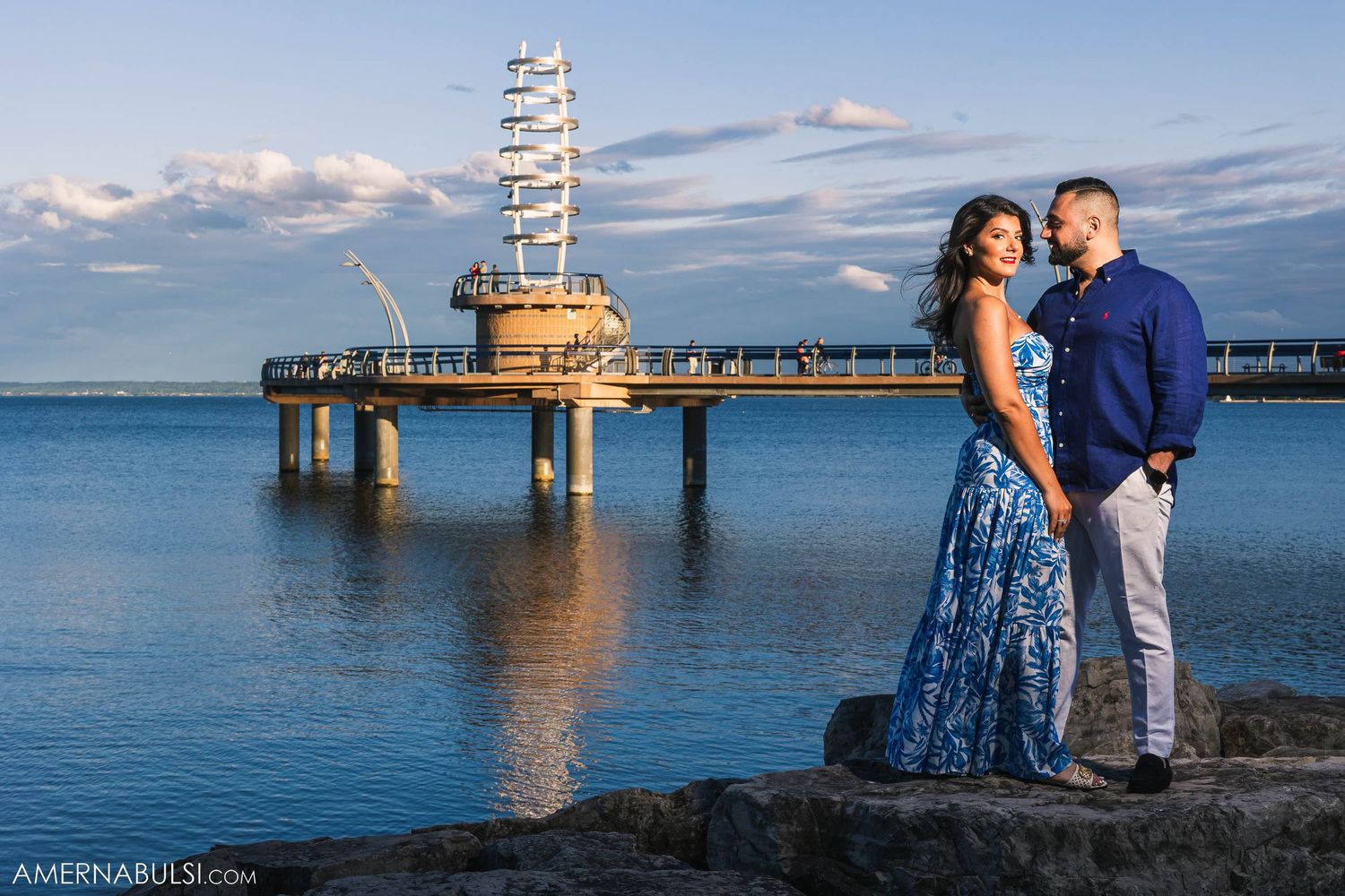 Couple poses by distinctive architectural pier structure over calm blue waters.