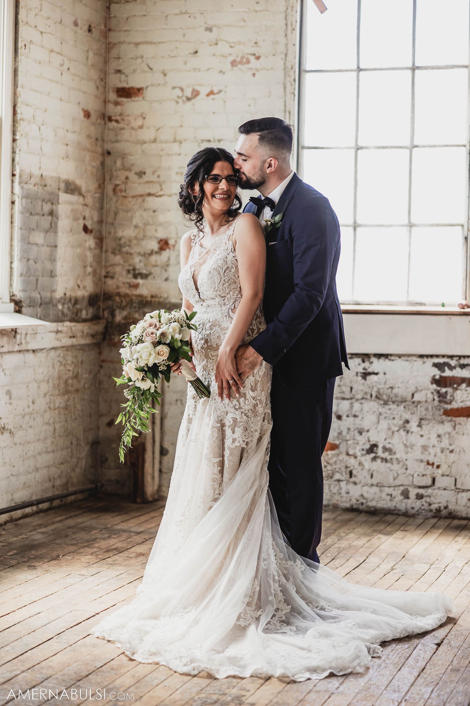 Couple shares intimate moment in industrial venue with exposed brick and natural light.