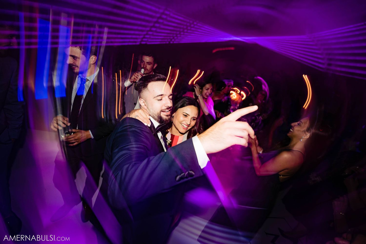 Wedding celebration with dancing guests under vibrant purple and blue lighting.