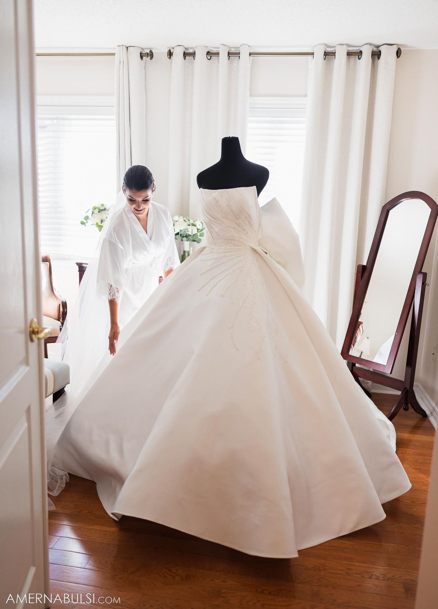 A stunning white wedding dress on a mannequin with elegant draping and full skirt in a bright room.