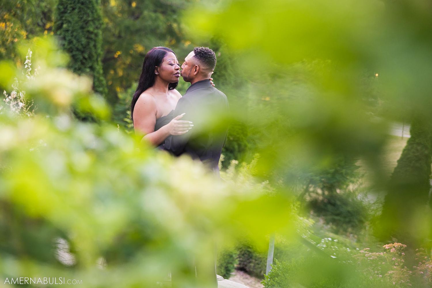 Romantic portrait through greenery of couple in formal attire.