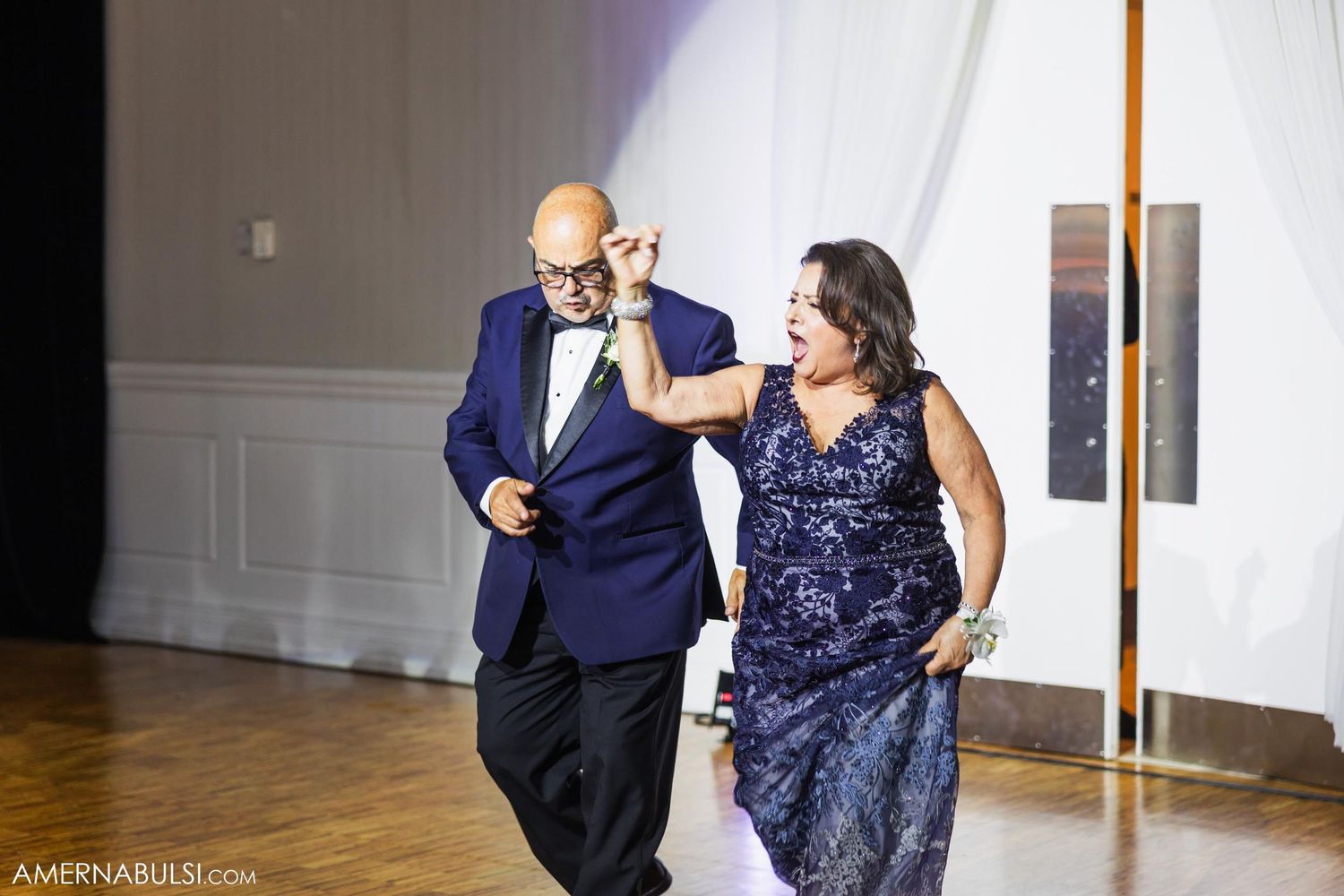 Formal couple in navy and sparkly attire make entrance at wedding reception.