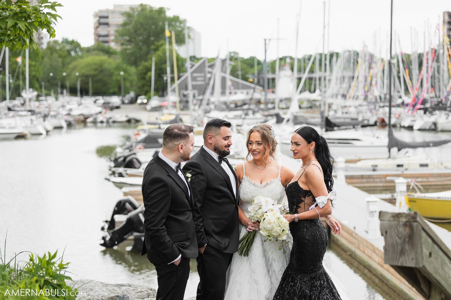 Wedding party poses by marina with boats and docks in background.
