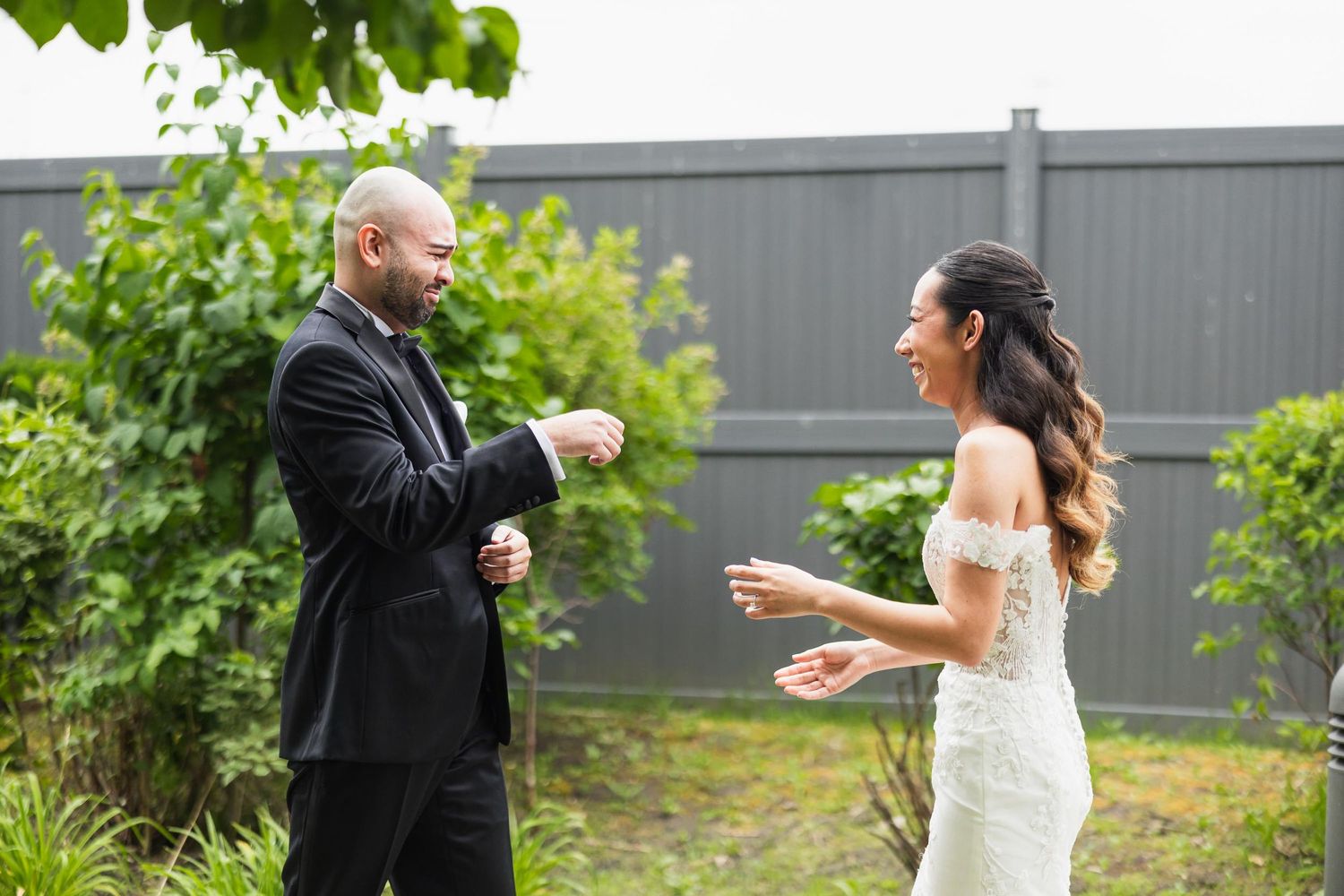 Playful moment between wedding couple gesturing and laughing in outdoor garden setting.