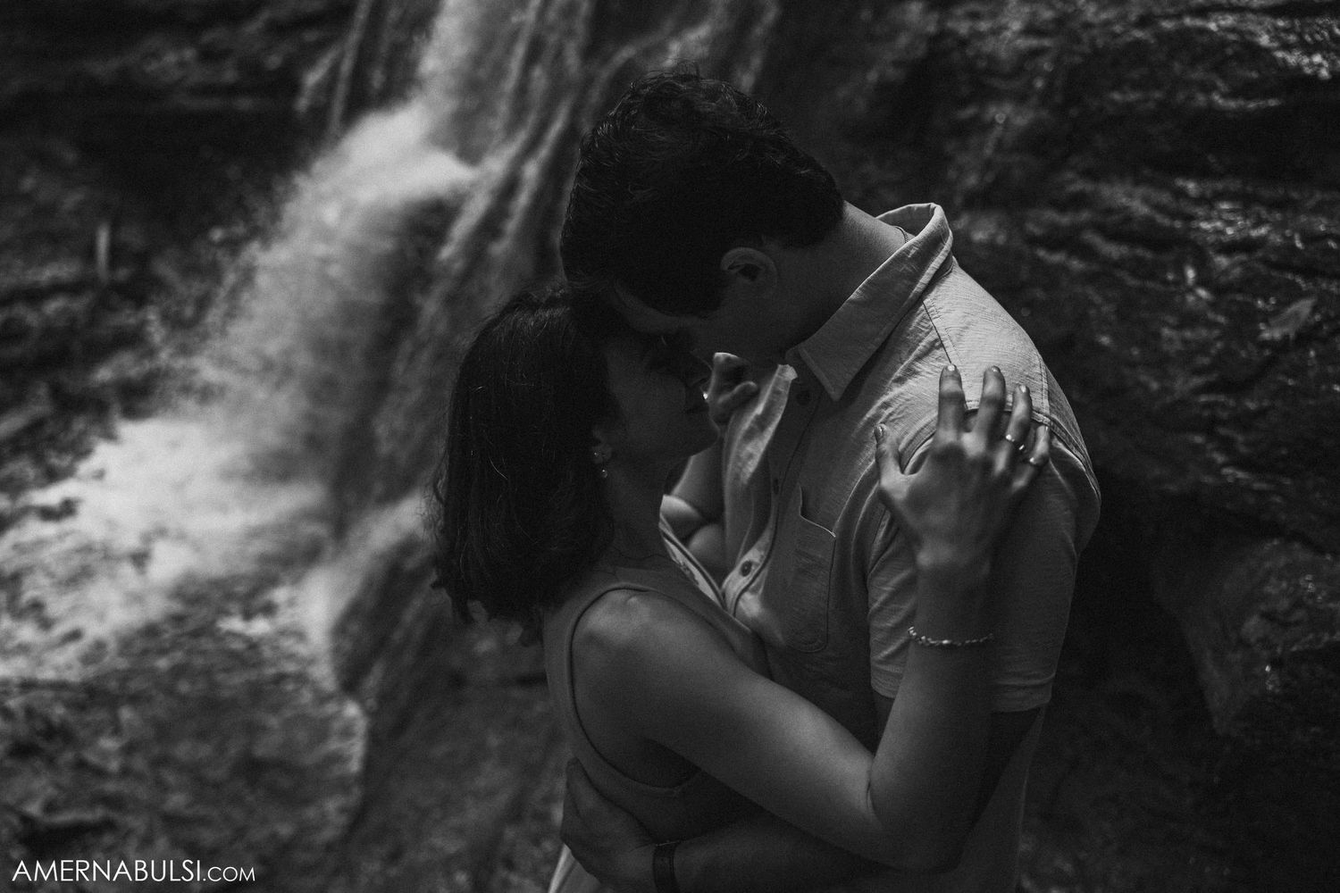 A romantic moment captured in black and white by a waterfall.