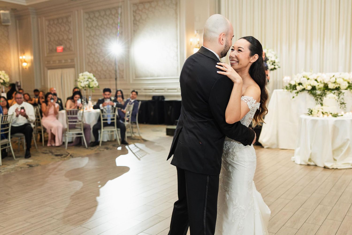 A couple shares an emotional moment during their wedding dance in an elegantly decorated ballroom.