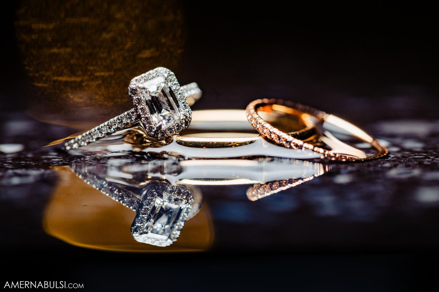 Wedding rings displayed artistically with reflections on dark surface.