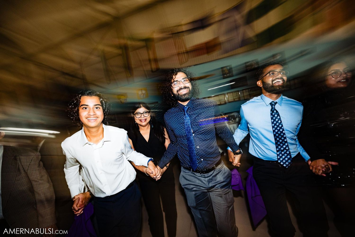 Wedding guests dancing and celebrating with dynamic motion blur in a dark reception venue.