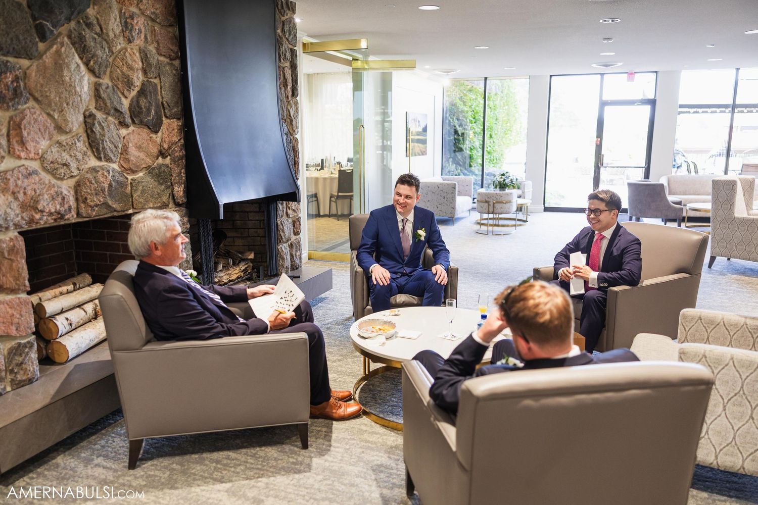 Wedding party relaxes in modern lounge area with stone fireplace.