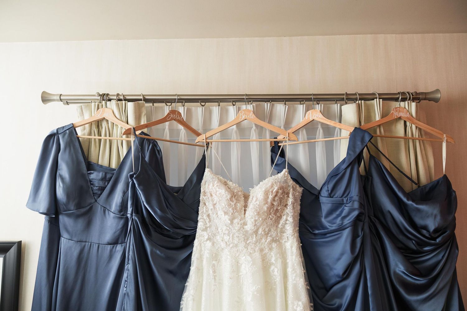 Wedding party attire displayed with white bridal gown and navy blue bridesmaid dresses hanging on rod.