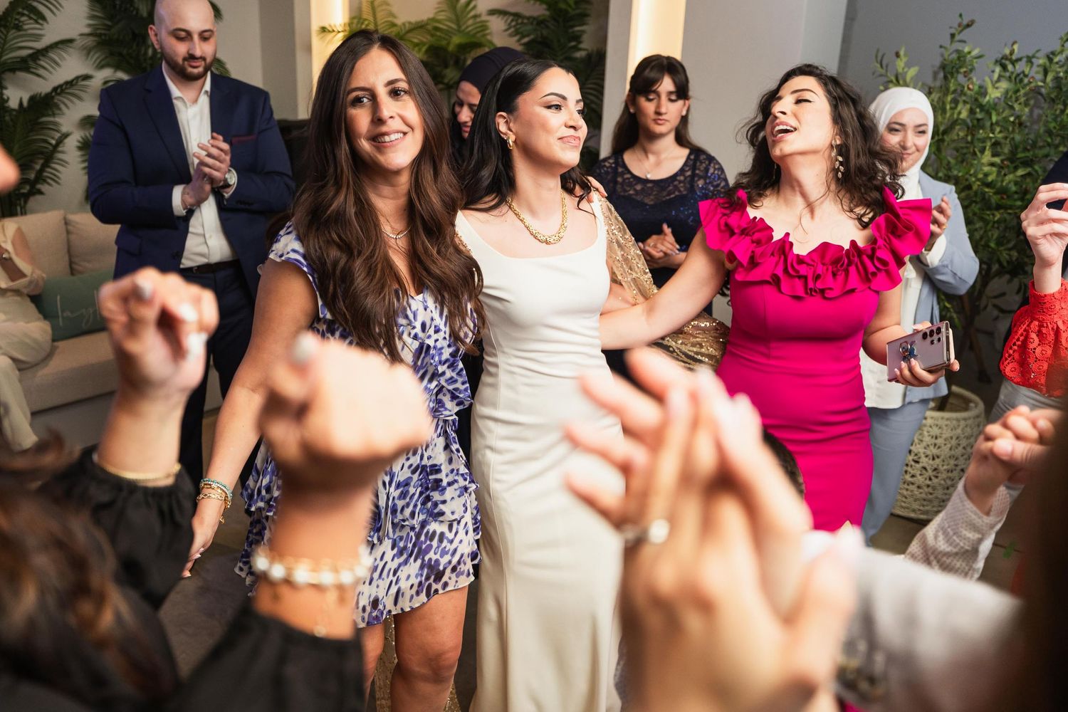 Guests in colorful dresses dance and celebrate at a festive indoor event.