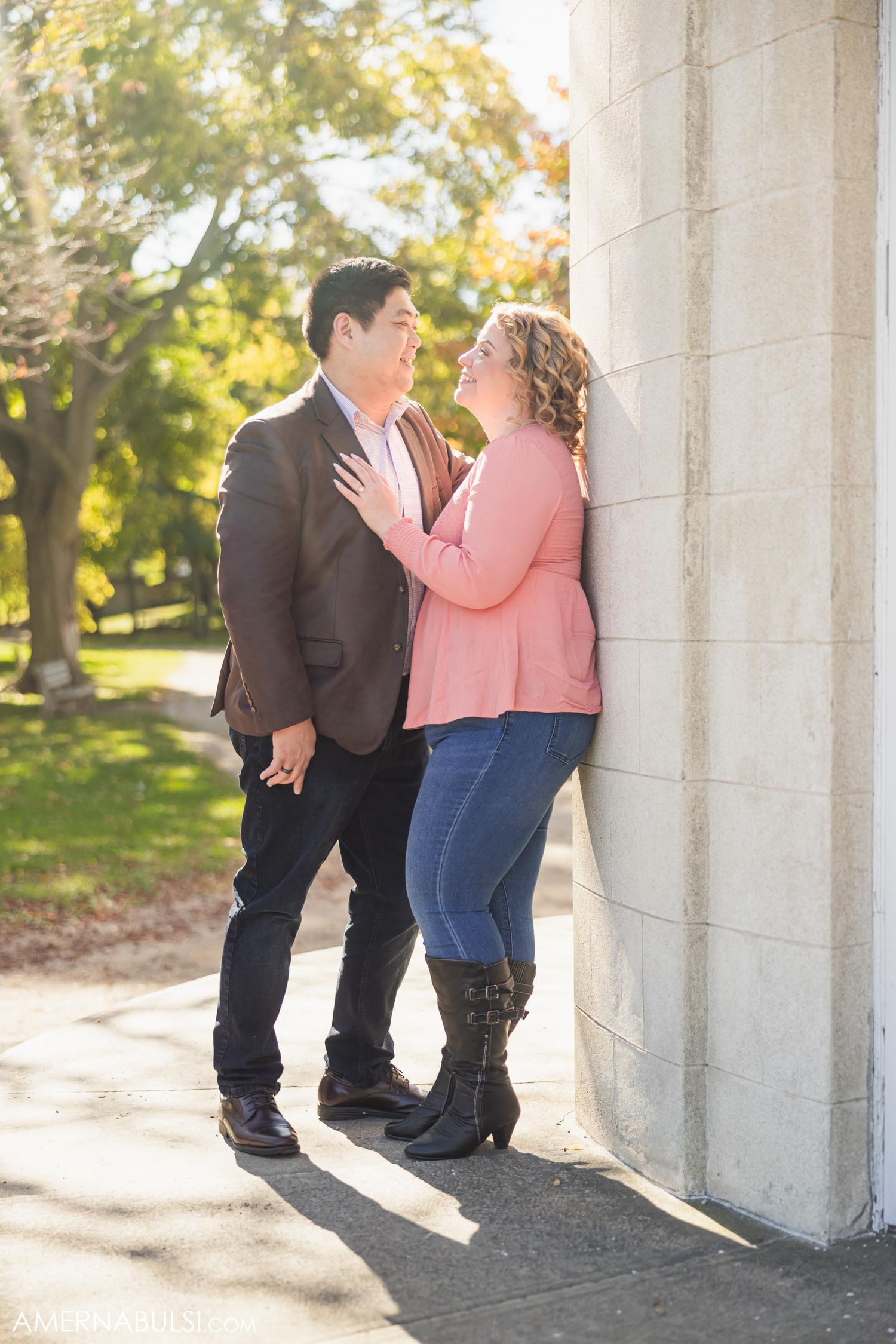 Intimate couple moment against white stone wall with autumn trees in background.