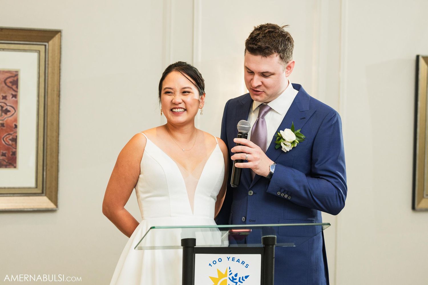 Newlyweds share joyful laughter while giving wedding speeches at reception podium.