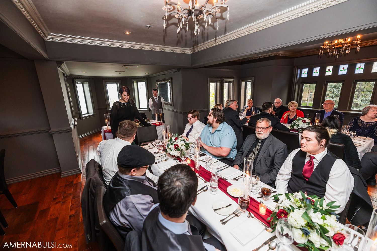 Wedding reception dining room with guests seated at long tables under crystal chandeliers.