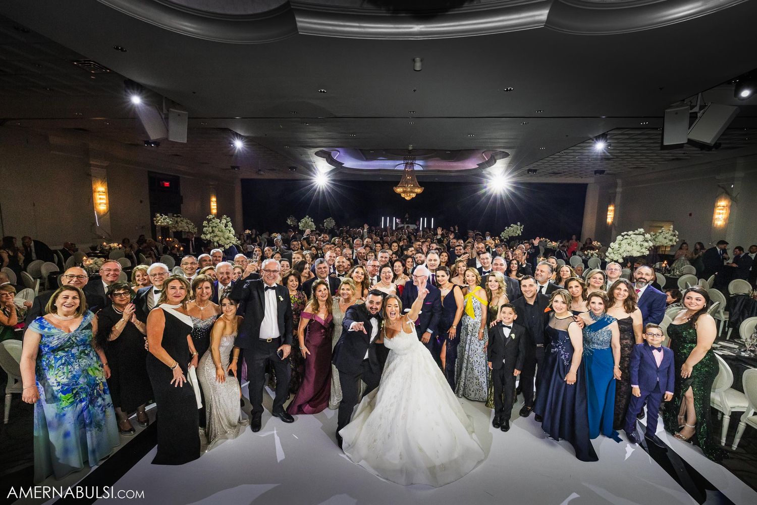 Wide shot of wedding reception with large crowd gathered on dance floor under elegant lighting.