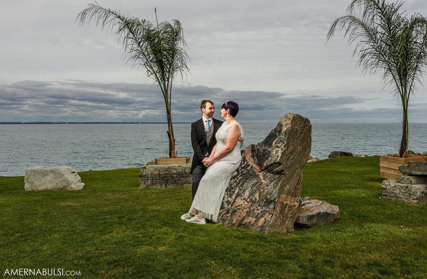 Coastal wedding portrait with couple posed near large rock formation and palm trees.