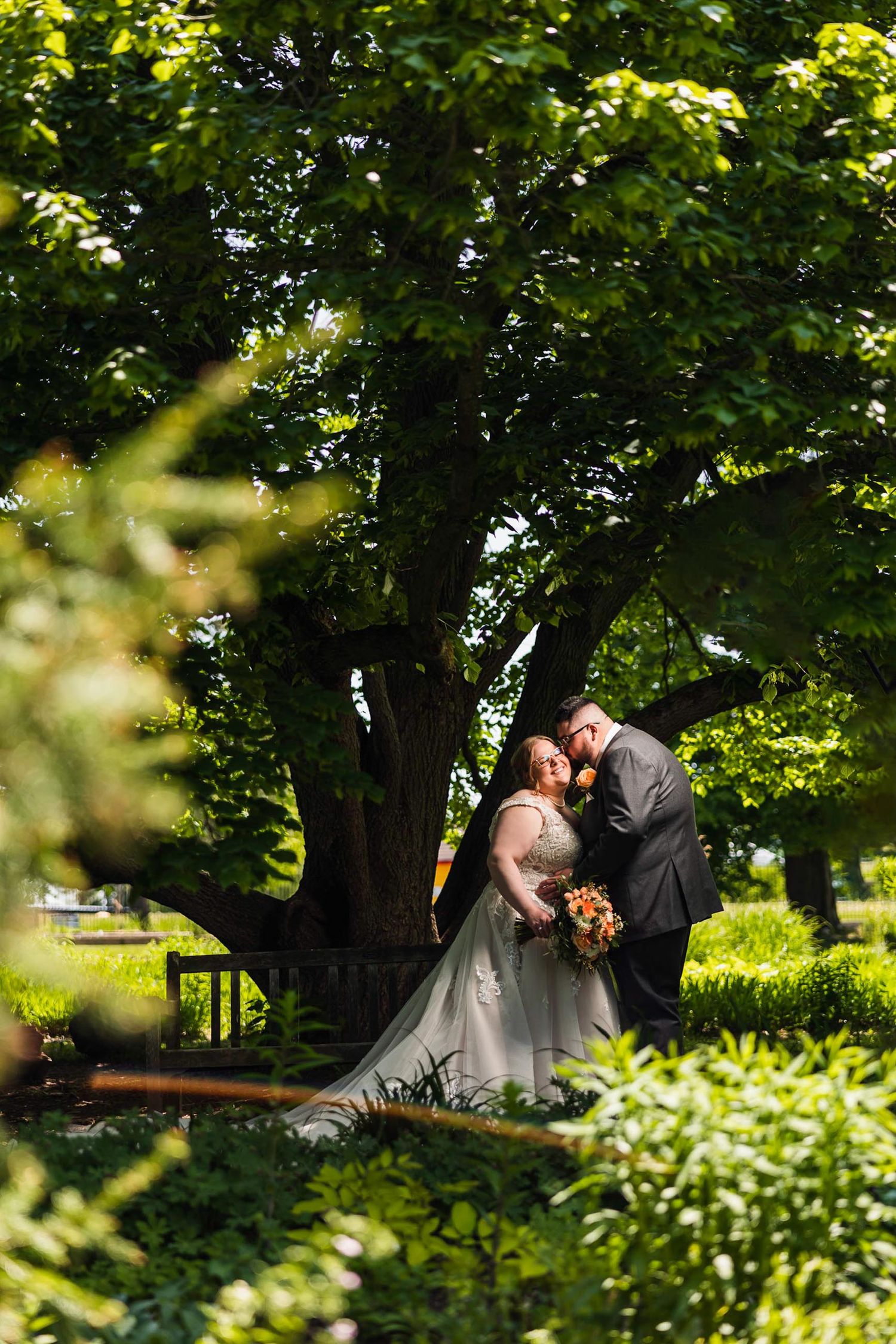Romantic wedding portrait through trees with couple in garden setting.