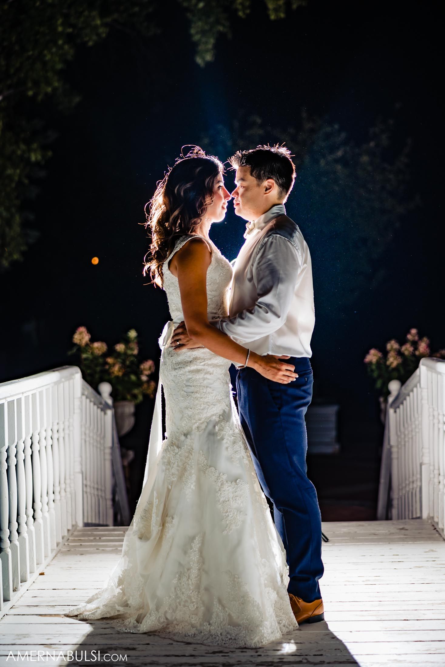 A romantic moment between dancers on an illuminated white bridge at night.