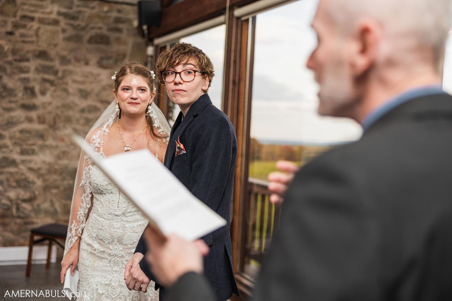 A wedding ceremony moment unfolds in a rustic venue with stone walls.
