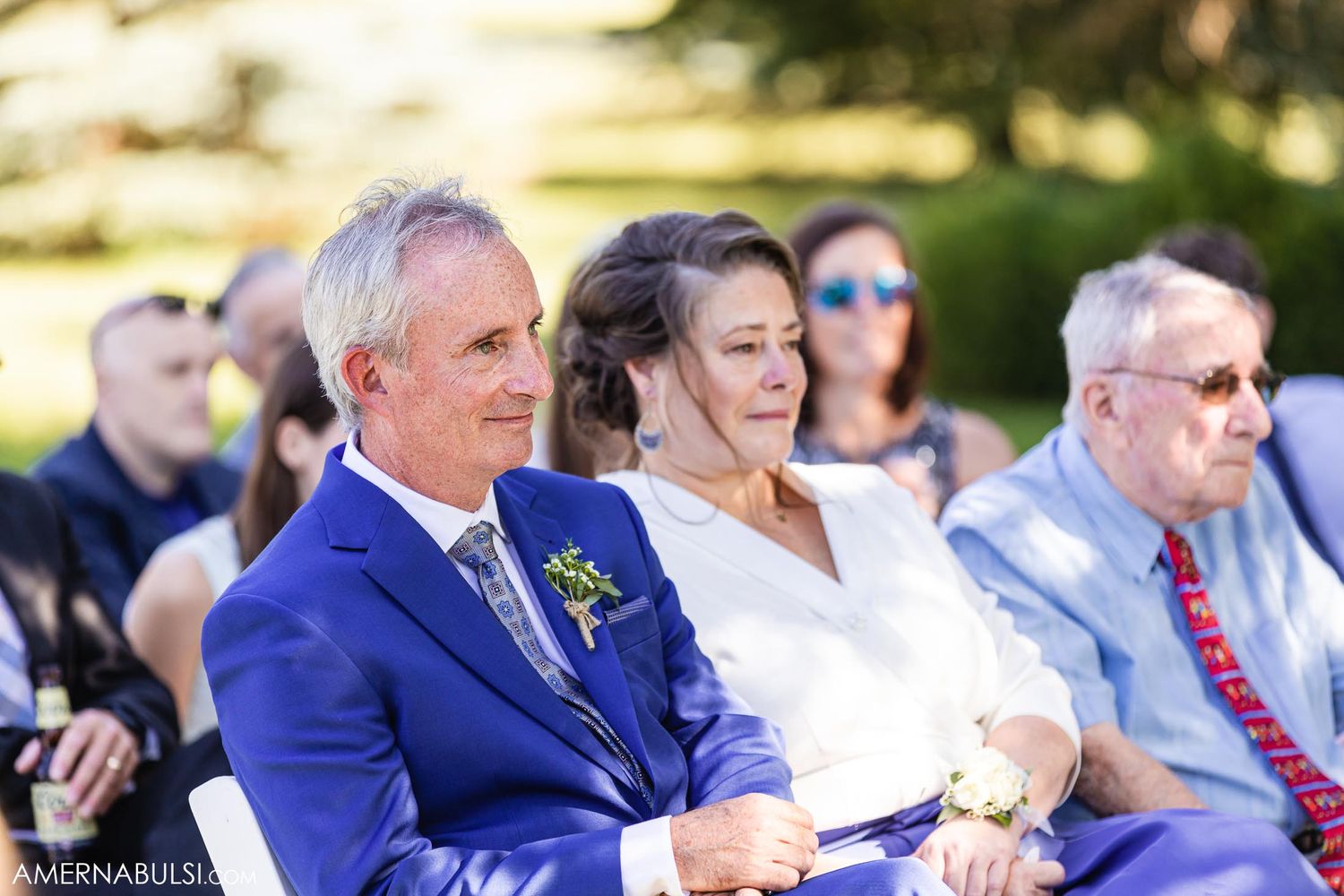 Wedding guests seated outdoors watching ceremony under bright summer sunshine.