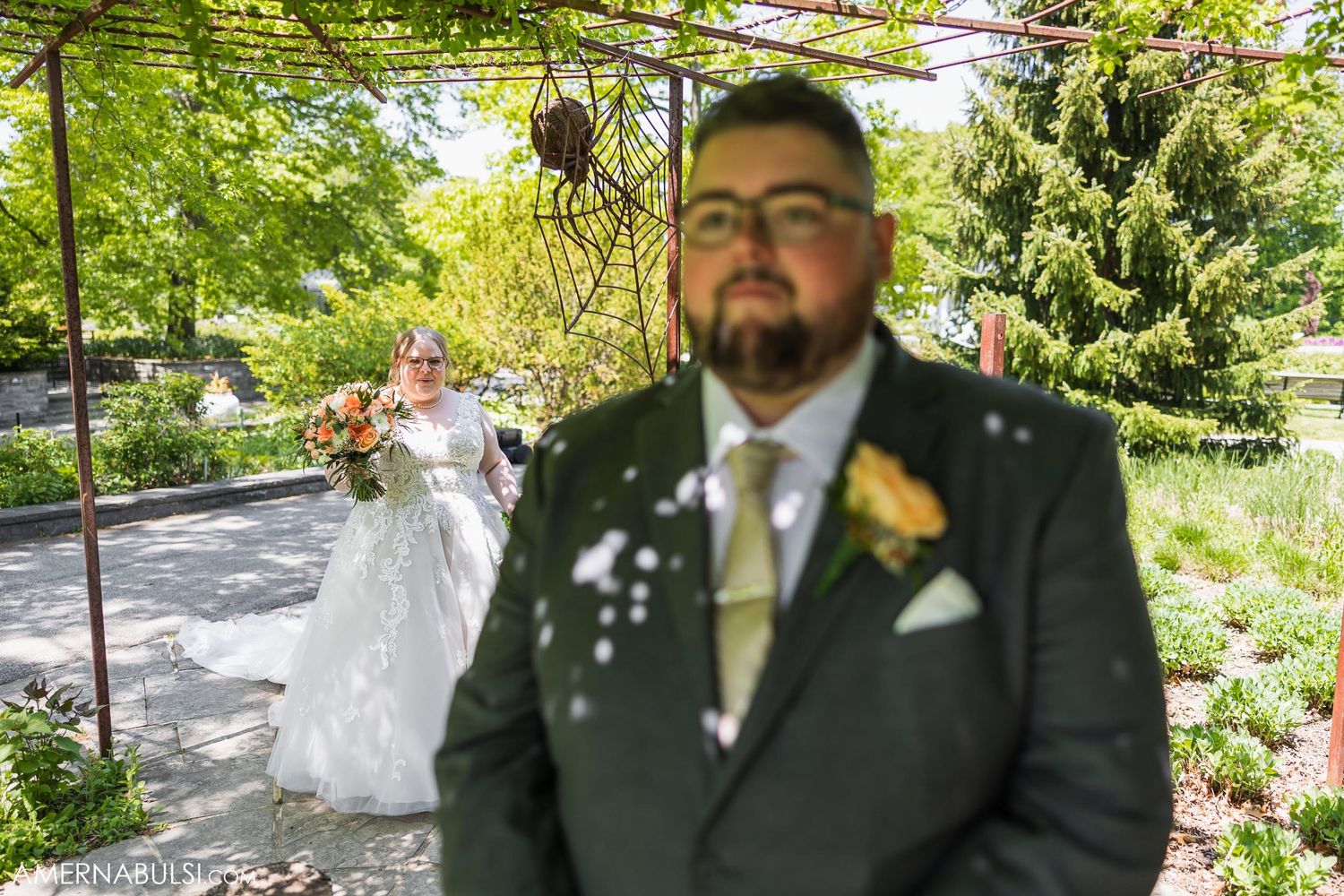 Wedding portrait through floral archway in scenic garden setting.