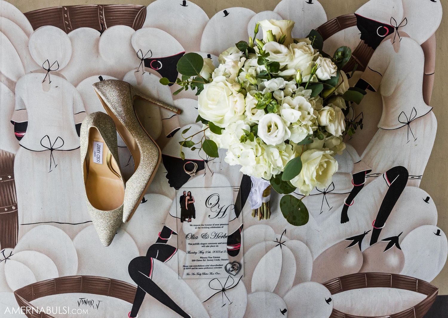 Wedding details flat lay featuring white roses, bridal shoes and invitation on patterned background.