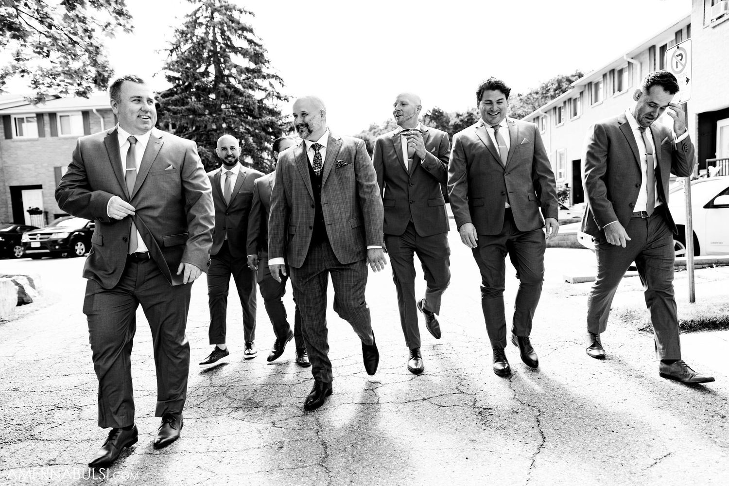 Black and white photo of groomsmen walking in coordinated suits on a sidewalk.