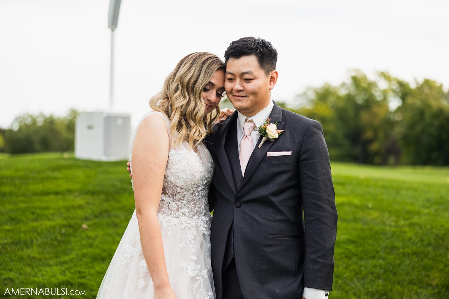 Intimate moment between couple on grassy hill during wedding day.