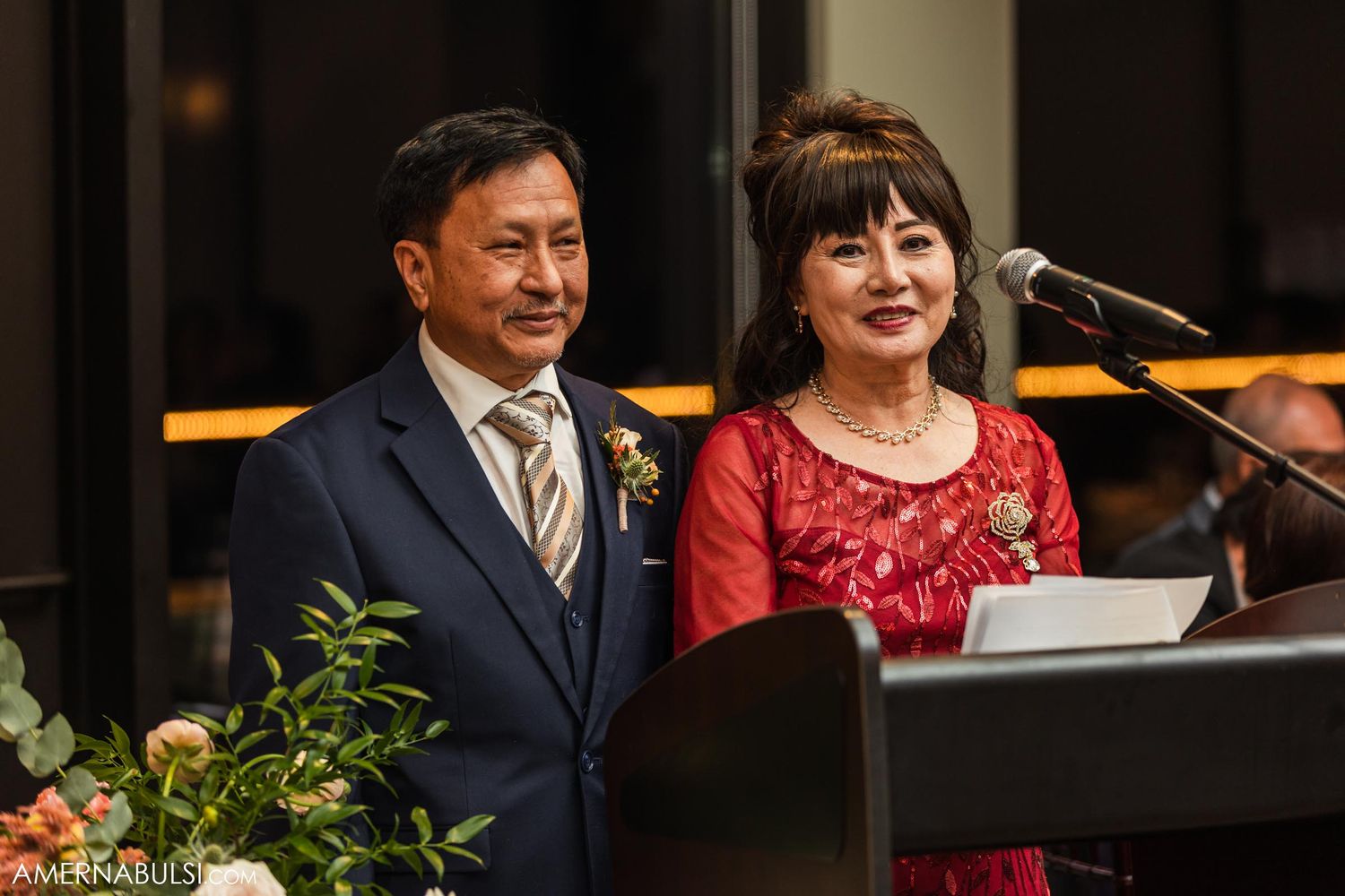 A couple dressed in formal attire stands at a podium during an evening event.